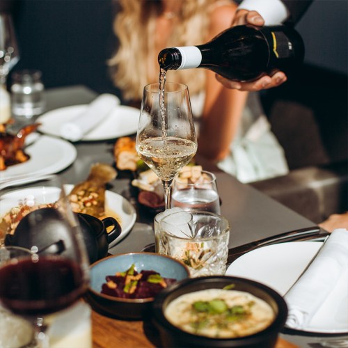 White wine being poured into a glass, surrounded by several different dishes on the table.